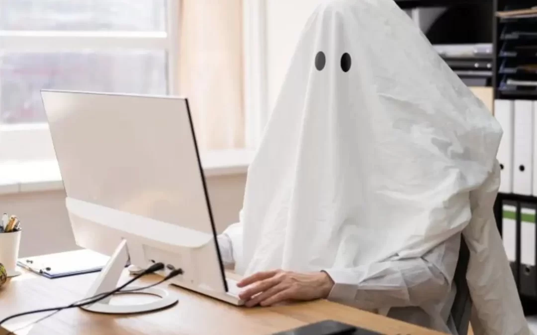 A person dressed in a ghost costume, sitting at a desk and typing on a computer.