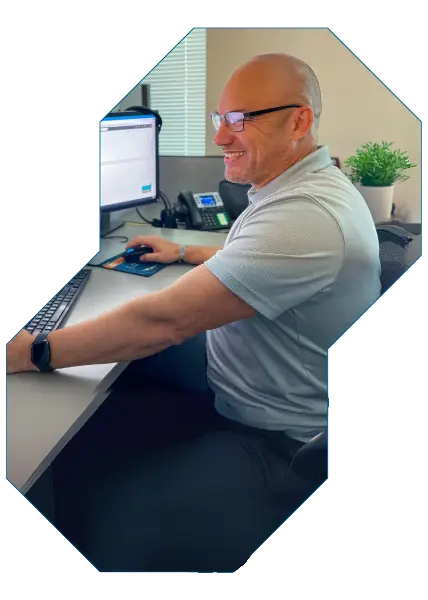 image of wingswept employee smiling while working on a computer in the office at his cubicle