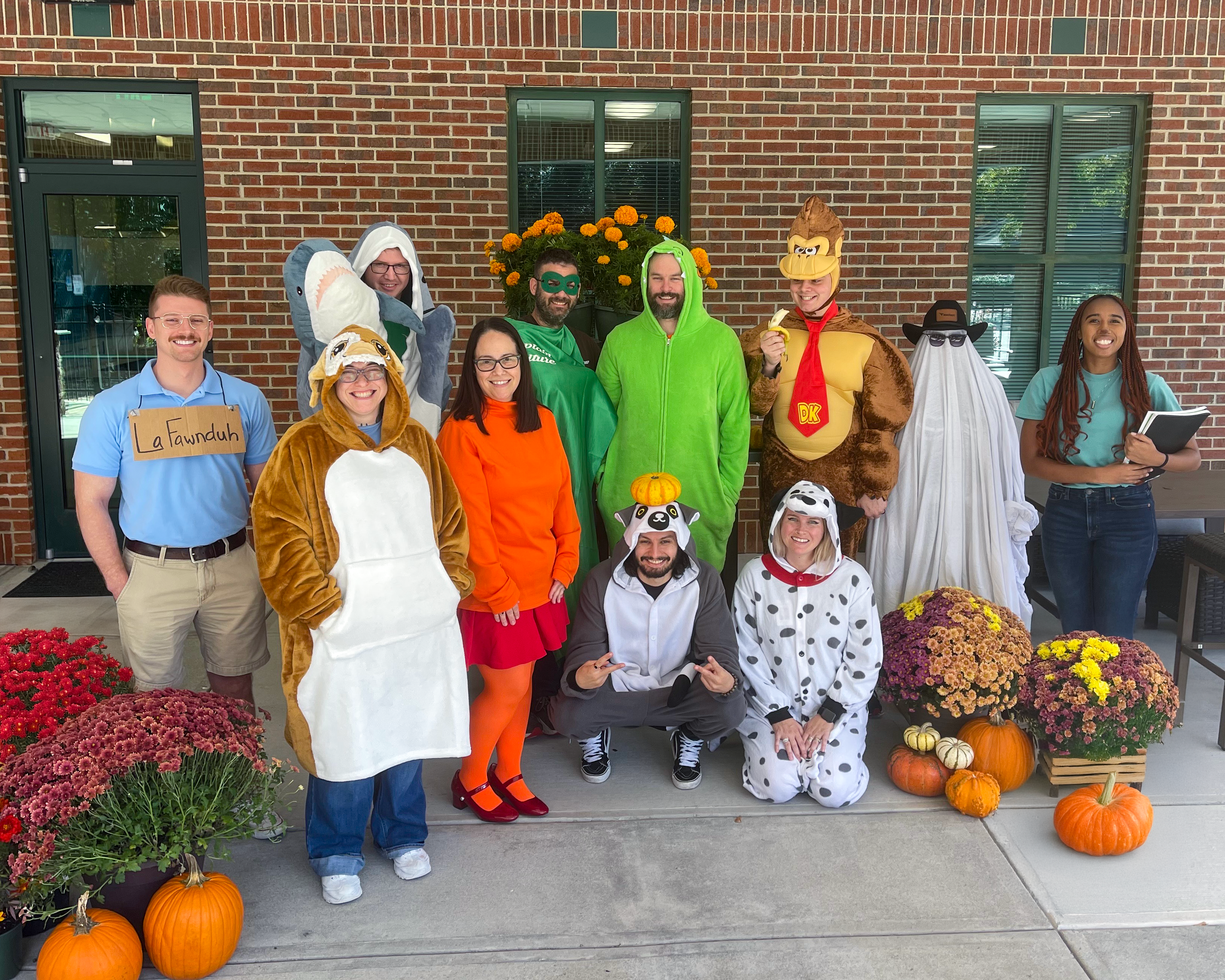 Eleven team members dressed in creative and festive Halloween costumes, posing together with smiles.