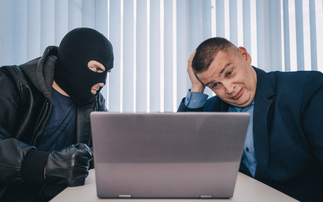 A concerned man sitting at a desk with a laptop, facing a masked individual in black gloves, depicting a cybersecurity threat or data breach scenario.